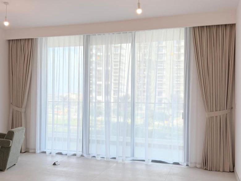 Sheer curtains with a wave heading across a wide living room window, with side curtains tied back at each end