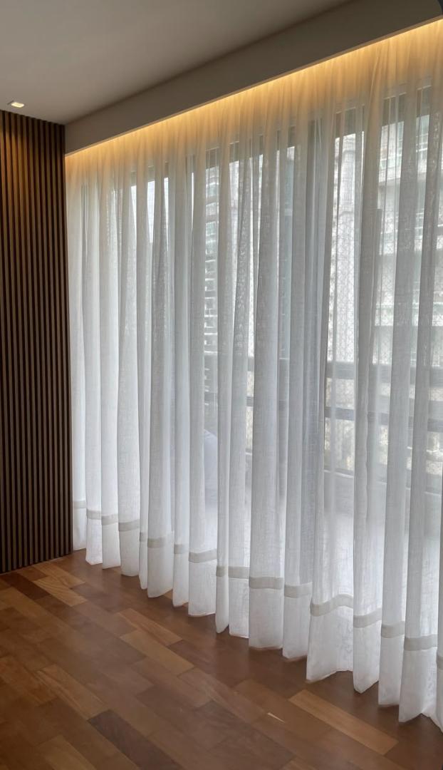 White voile sheer curtains in wave folds on a ceiling track across a floor-to-ceiling glazed wall, beside a dark timber slat wall