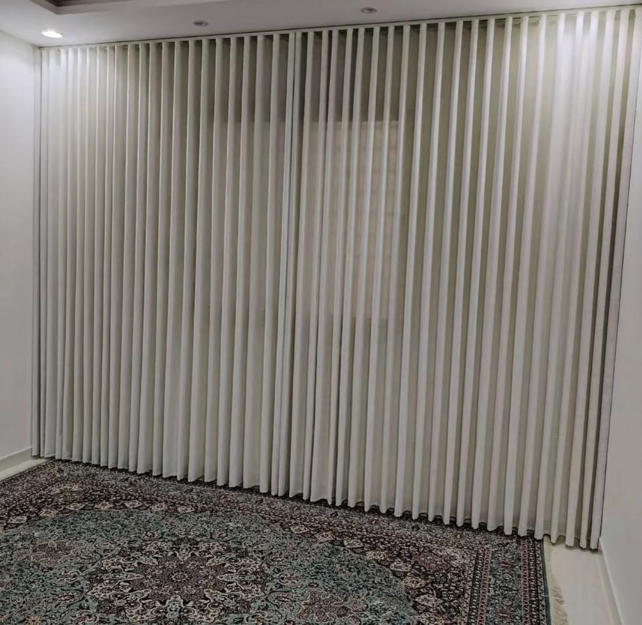 Off-white wave curtains drawn closed around a corner run of windows above a patterned rug in an empty room