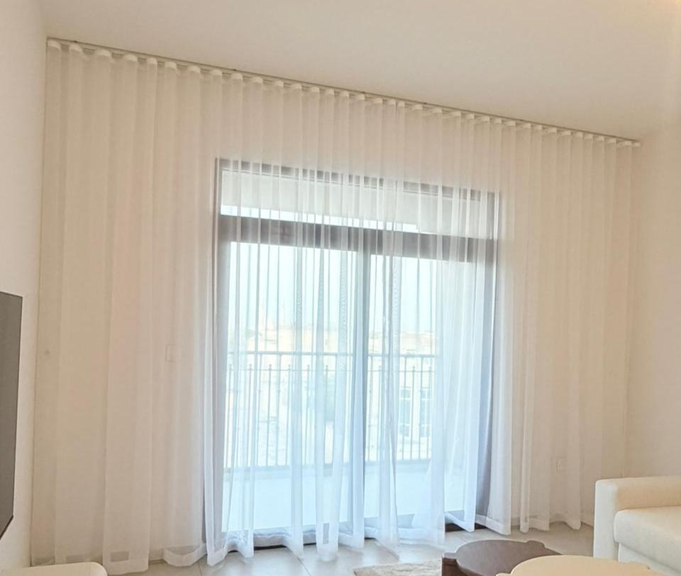 Cream sheer curtain on a ceiling track with gliders visible