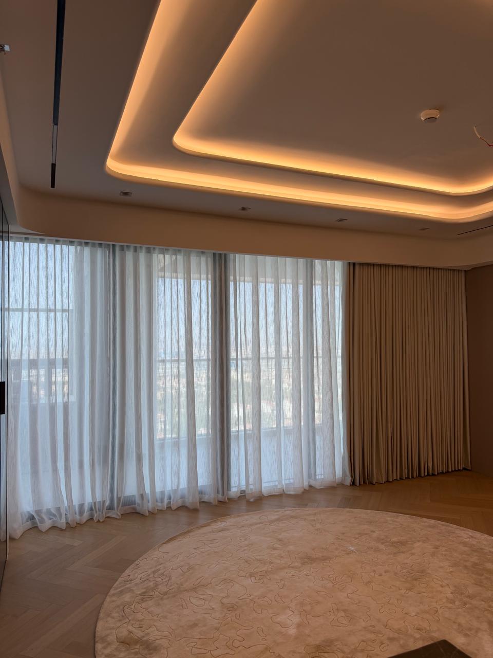 Sheer and taupe curtains under a cove-lit ceiling in a living room