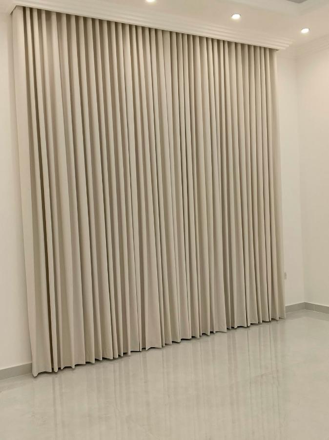 Cream heavy curtains drawn fully closed along a wall from a recessed ceiling track, in an empty room with a polished marble floor