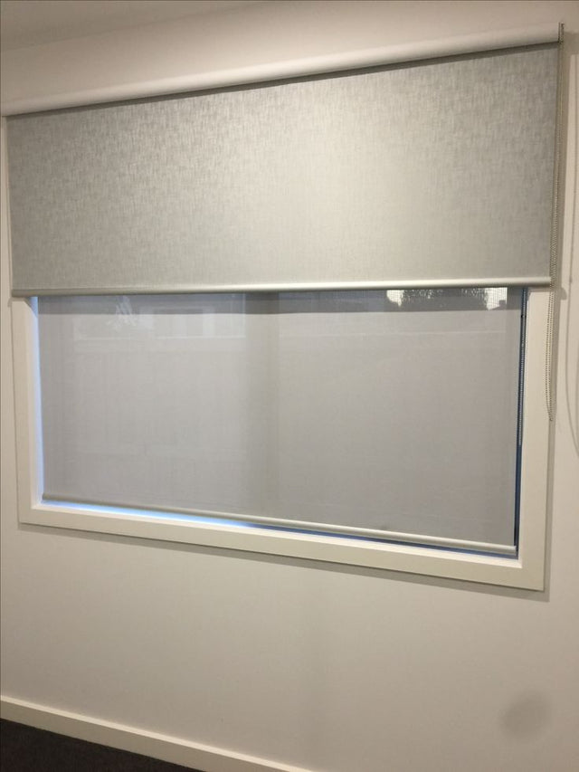 Grey roller blind half lowered inside a white window recess