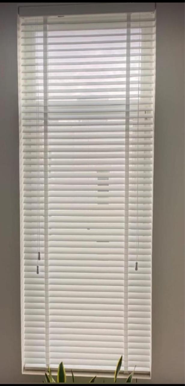 White aluminium venetian blind with the slats closed on a tall narrow window