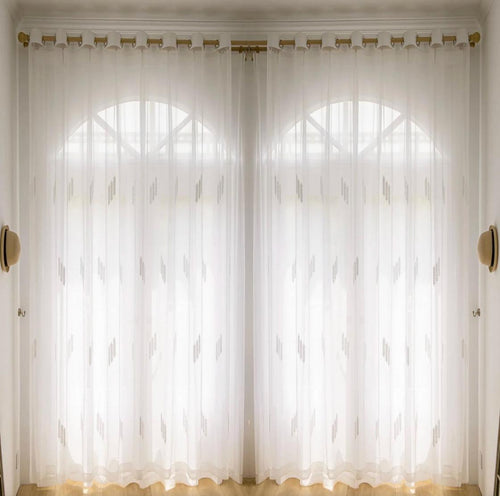 Embroidered sheer curtains with a leaf-sprig motif across two arched windows, held back by gold holdbacks