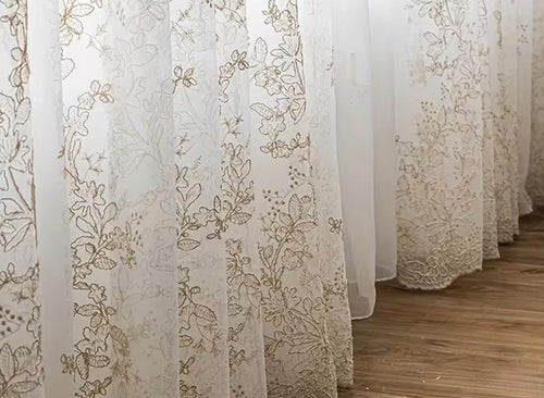 Embroidered sheer panels with gold floral and butterfly motifs and a scalloped lace border, hanging side by side on a rail