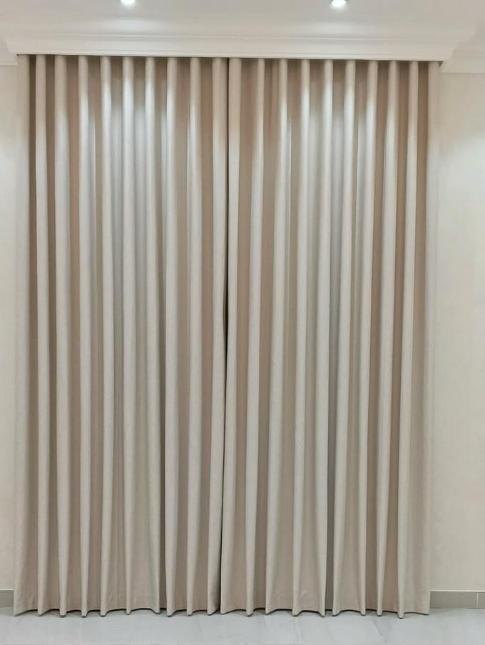 Taupe curtains drawn fully closed across a window from a plastered pelmet, passing no daylight, in an empty room